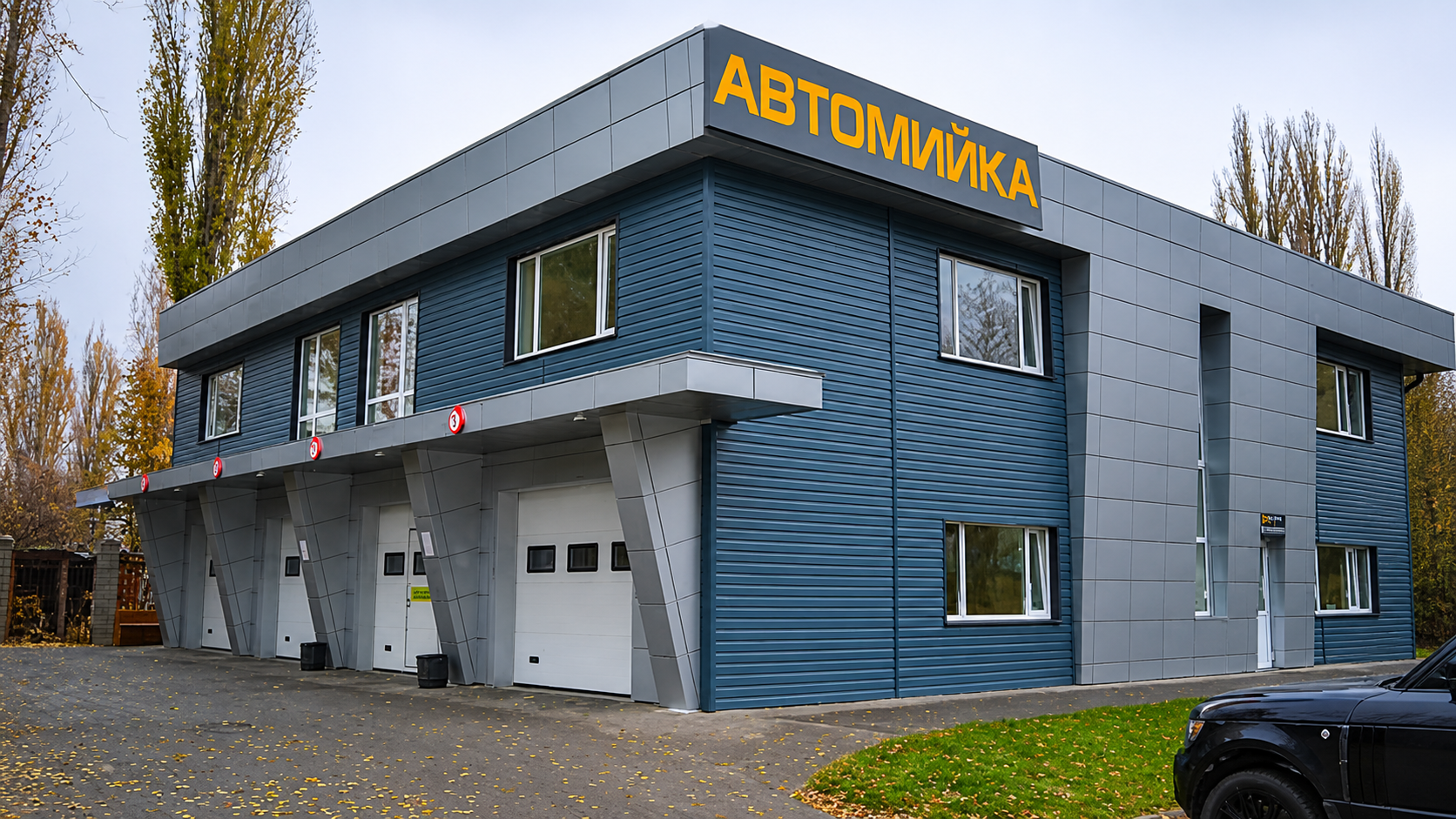 Современная автомойка с тремя боксами Современное двухэтажное здание автомойки с тремя воротами, серо-синим фасадом и вывеской «АВТОМИЙКА»