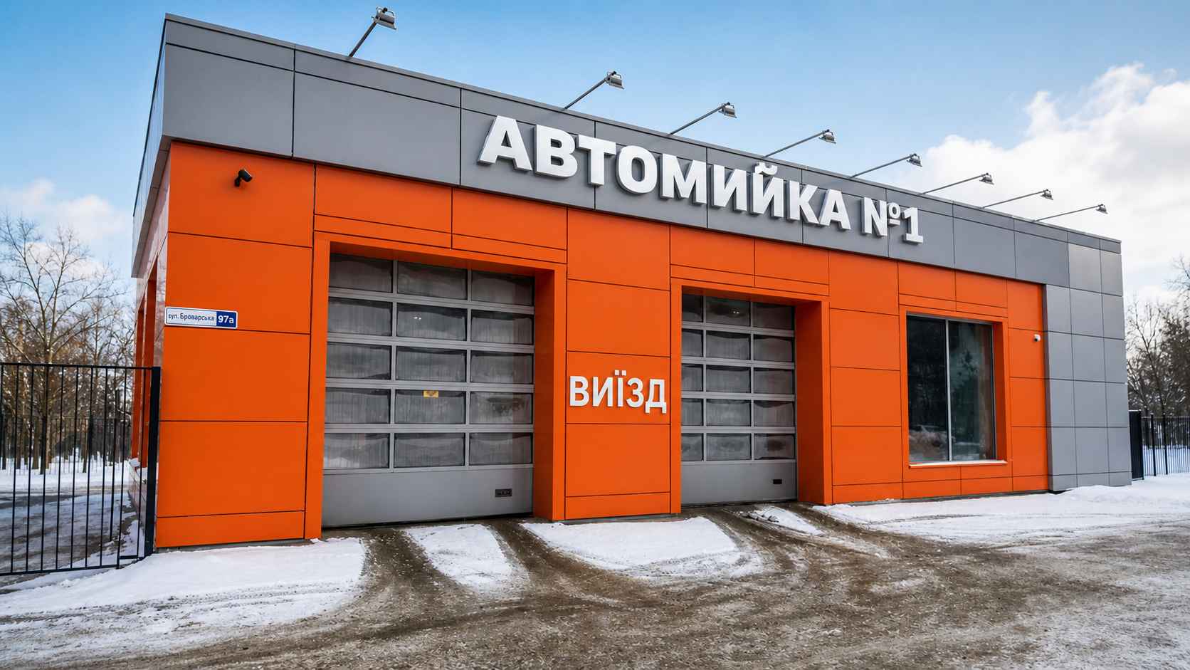 Автомойка №1 с оранжевым фасадом Современное здание автомойки №1 с ярким оранжевым фасадом, двумя въездными воротами и снежной территорией перед входом