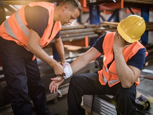 Manual worker assisting his colleague with physical injury in steel mill. Manual worker feeling pain after having an injury at work while his colleague is helping him.